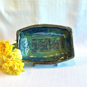 May include: A rectangular ceramic tray with a glossy, multi-toned glaze in shades of deep blue and forest green. The center of the tray features an embossed floral pattern. The edges are slightly raised, and the surface has a reflective finish.