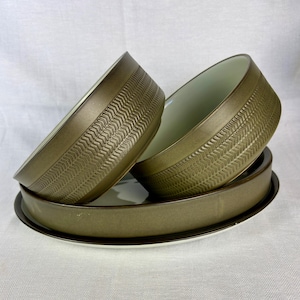 May include: A set of olive-green ceramic bowls and plates. The bowls have a textured, patterned band around the exterior. The plates are round with a dark brown rim and a white interior. The bowls are stacked on top of the plates.