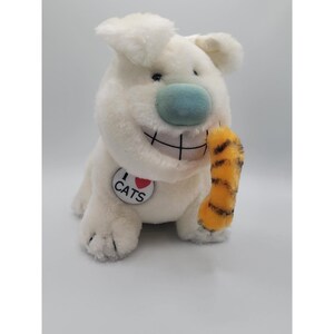 May include: A plush white dog toy with a blue nose and a large grin. The dog is holding a yellow and orange striped object. A circular tag on the dog says "I ❤️ CATS".