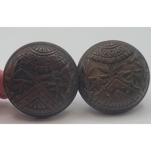 May include: Two antique bronze-colored cabinet knobs with intricate carved floral and geometric patterns. The knobs are round with a detailed design featuring leaves and symmetrical shapes, perfect for vintage furniture restoration.