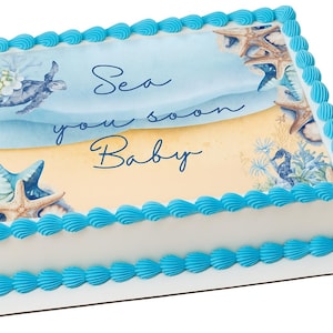 May include: A rectangular cake with white frosting and blue piped borders. The top features a beach scene with a turtle, starfish, and seahorse. The words "Sea you soon Baby" are written in script.