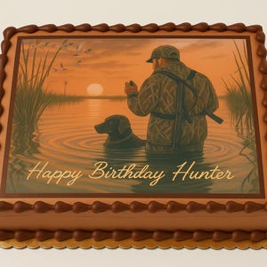 May include: A rectangular cake with a brown border and a gold base. The cake features an edible image of a hunter with a dog in a lake at sunset, with the text "Happy Birthday Hunter".