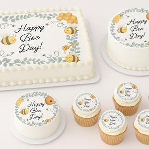 May include: A rectangular cake, a round cake, and cupcakes with white frosting. The cakes and cupcakes are decorated with a bee-themed design and the text "Happy Bee Day!" in black script. The design includes bees, honeycombs, and honey pots.