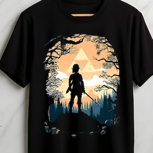 Peut inclure: T-shirt noir avec une silhouette d'une figure avec une épée, debout sur une colline, encadrée par une forêt et un coucher de soleil. Le design comprend un symbole triangulaire. Le t-shirt est suspendu à un cintre en bois.