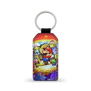 Peut inclure: Un porte-clés rectangulaire avec un anneau argenté et une sangle noire, représentant une illustration colorée de Mario et d'autres personnages de la série de jeux vidéo Paper Mario. L'arrière-plan est une scène du jeu.