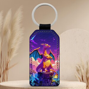 May include: A rectangular keyring with a metal ring and a black strap. The keyring features a vibrant illustration of a purple and yellow dragon with blue wings against a purple and blue night sky background.