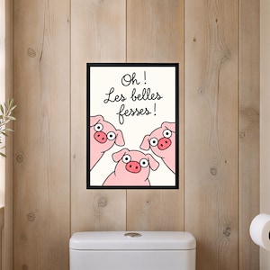 Peut inclure: Une affiche encadrée représentant trois cochons roses de dessin animé aux yeux écarquillés regardant vers le haut. Le texte "Oh ! Les belles fesses !" est écrit en écriture cursive noire au-dessus des cochons sur un fond crème.