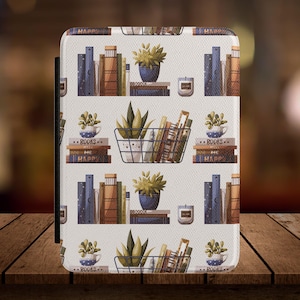 May include: A white e-reader case featuring a repeating pattern of books, potted plants, and candles. The design includes stacks of books in various colors, small blue pots with plants, and a wire basket filled with books. The words "BOOKS ME HAPPY" are visible.