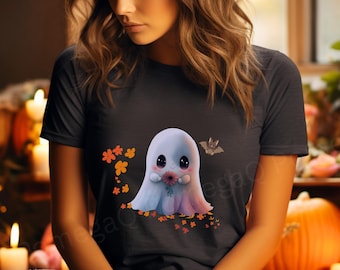 May include: A dark gray t-shirt featuring a cute ghost illustration holding a flower, with a bat and orange flowers. The ghost has large black eyes and a soft, colorful gradient. The shirt is a casual, everyday wear item.