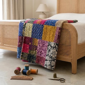 May include: A colorful patchwork quilt with squares of various fabrics in shades of blue, yellow, pink, and black, draped over a light wood bed frame. Spools of thread and a wooden comb are on the floor.