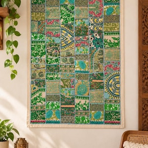 Peut inclure: Une tenture murale rectangulaire composée d'un patchwork de carrés de tissu dans des tons de vert, bleu sarcelle et jaune. Le textile présente des broderies florales et géométriques complexes, avec une bordure en tissu beige clair.