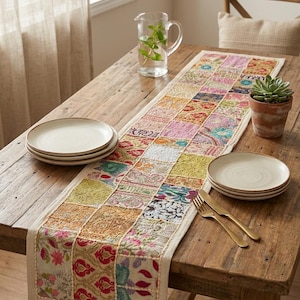 May include: A rectangular table runner featuring a patchwork design composed of various small, multi-colored fabric squares with intricate floral and geometric embroidery patterns, finished with a solid cream-colored border along the edges.