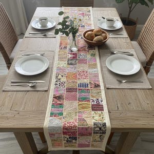 May include: A dining table set for a meal, featuring a patchwork runner, white plates, and silverware. A vase of flowers and a bowl of bread are on the table. Wicker chairs surround the wooden table. The table setting includes small cups.