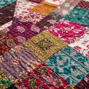 Puede incluir: Una colcha de patchwork compuesta por diversos parches de tela cuadrados en colores variados como rojo oscuro, amarillo mostaza, azul verdoso y morado. Cada cuadrado muestra distintos patrones florales, de cachemira y geom&eacute;tricos con puntadas blancas.