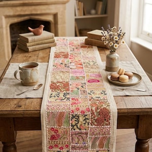 May include: A rectangular table runner featuring a patchwork design of embroidered fabric squares in shades of pink, green, gold, and cream. The runner displays intricate floral and paisley patterns with detailed stitching throughout the textile surface.