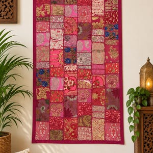 Puede incluir: Un tapiz rectangular con un diseño de patchwork compuesto por varios cuadrados de tela en tonos rosa, magenta y rojo. El tejido muestra diversos patrones, incluyendo motivos florales, bordados metálicos y texturas tejidas complejas.