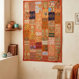 Puede incluir: Un tapiz rectangular con un diseño de patchwork de varios cuadrados de tela en tonos naranja, dorado, azul y verde. El tejido muestra bordados intrincados, detalles en hilo metálico y diversos patrones florales y geométricos.