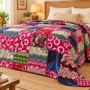 Op de afbeelding: Een patchwork sprei met een levendige mix van magenta, donkerrode, marineblauwe en groene stoffen vierkanten. Elk vierkant toont verschillende witte en veelkleurige bloem-, geometrische en cirkelvormige patronen met zichtbare stiksels.