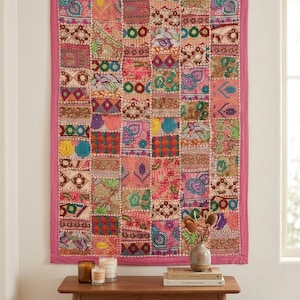 Könnte beinhalten: Ein rechteckiger Wandbehang mit einem Patchwork-Design aus verschiedenen Stoffquadraten in Rosa-, Orange-, Grün- und Blautönen. Das Textil ist mit aufwendigen Stickereien, Pailletten und Perlen verziert und mit einem einfarbigen rosa Rand versehen.