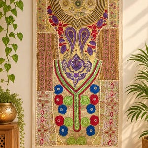 Puede incluir: Un tapiz rectangular que presenta un mosaico de paneles de tela bordada en amarillo, rosa y dorado. El diseño incluye intrincados abalorios, motivos de cachemira morados y una disposición vertical central de aplicaciones florales azules y verdes.