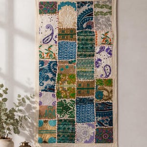 Könnte beinhalten: Ein rechteckiger Wandbehang mit einem Patchwork-Design aus verschiedenen Stoffquadraten. Das Textil zeigt eine vielfältige Farbpalette in Blau, Grün, Gold, Lila und Weiß, ergänzt durch aufwendige Stickereien, Pailletten und Paisley-Muster.