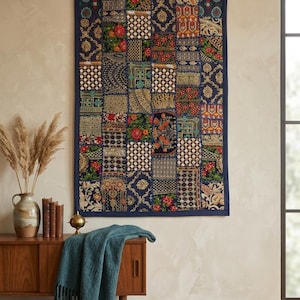 May include: A rectangular wall hanging featuring a patchwork design of various dark blue fabric squares with intricate gold, red, and green floral and geometric embroidery patterns, finished with a solid dark blue fabric border around the edges.