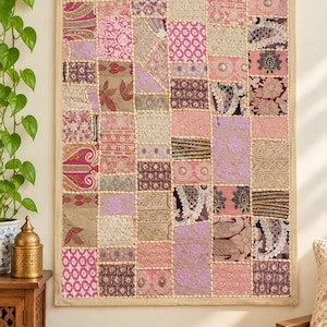 Peut inclure: Une tenture murale rectangulaire présentant un motif en patchwork composé de divers carrés de tissu dans des tons de rose, mauve et beige. Le textile comprend de multiples motifs floraux, géométriques et en dentelle, avec de petites perles blanches cousues le long des coutures.