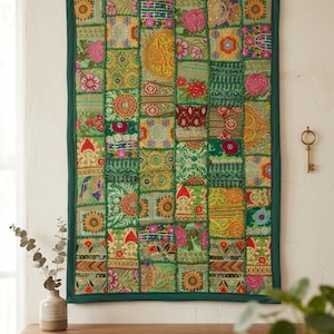 Könnte beinhalten: Ein rechteckiger Wandbehang aus einem Patchwork aus grünen Stoffquadraten mit aufwendigen Stickereien, Blumenmustern und Akzenten aus Metallfäden. Das Textil ist dunkelgrün umrandet und zeigt eine Vielzahl von farbenfrohen, detaillierten Mustern.