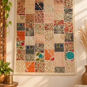 May include: A rectangular wall hanging featuring a patchwork design of various fabric squares. The textile displays a diverse array of floral, geometric, and abstract patterns in colors including orange, blue, green, cream, and dark brown.