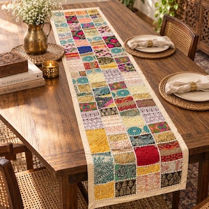 Puede incluir: Un camino de mesa rectangular largo con un diseño de patchwork compuesto por numerosos cuadrados de tela pequeños y multicolores. El camino muestra una variedad de patrones intrincados, texturas y tonos vibrantes que incluyen rojo, amarillo, azul y verde.