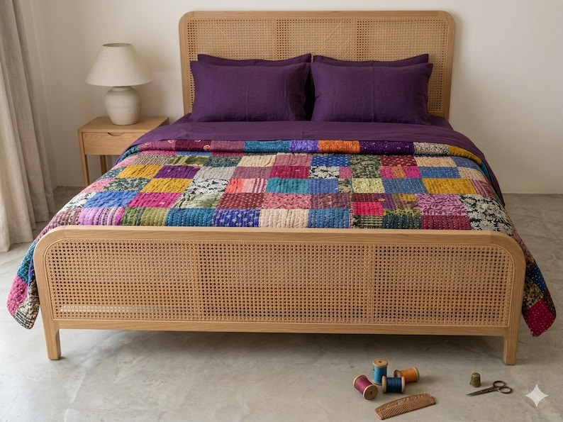 May include: A bed with a light wood frame and headboard, featuring a woven cane design. The bed is made up with purple sheets and a colorful patchwork quilt. A small side table with a lamp is visible in the background.
