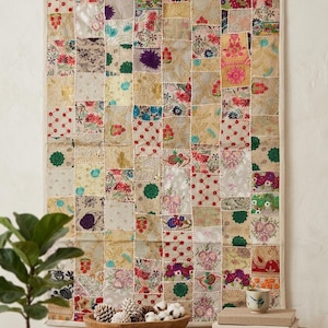 May include: A rectangular wall hanging featuring a patchwork design of various fabric squares. The textile displays a mix of floral patterns, metallic gold embroidery, and intricate beadwork in shades of red, green, blue, and cream.