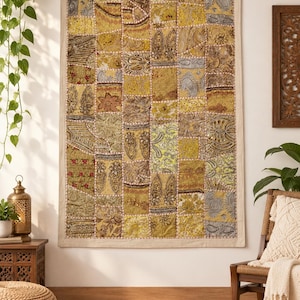 May include: A rectangular wall hanging featuring a patchwork design of various yellow, gold, and metallic silver fabric squares. The textile displays intricate embroidery, floral motifs, paisley patterns, and small reflective mirror accents.