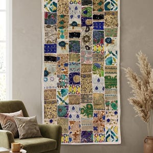 May include: A rectangular wall hanging featuring a patchwork design composed of numerous small, square fabric panels. Each panel displays distinct, intricate patterns, embroidery, and a vibrant colour palette including blue, gold, green, and white.