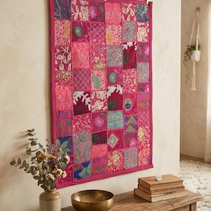 Pode incluir: Uma tapeçaria retangular composta por um mosaico de quadrados de tecido em tons de magenta, rosa e multicoloridos. Cada quadrado apresenta bordados intrincados, lantejoulas e missangas com padrões florais e paisley, com uma borda magenta sólida.