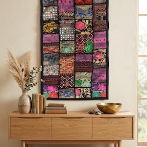 Könnte beinhalten: Ein rechteckiger Wandbehang aus einem Patchwork aus bestickten Stoffquadraten in leuchtenden Farben wie Rot, Pink, Blau, Grün und Gold. Die Textilkunst zeigt komplexe florale Muster, geometrische Formen und Akzente aus metallischen Fäden.