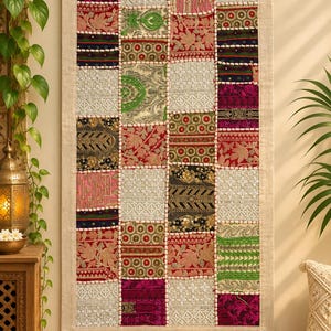 Peut inclure: Une tenture murale rectangulaire composée d'un patchwork de carrés de tissu brodés dans des tons de rouge, vert, noir, rose et crème. Les carrés sont séparés par une bordure perlée blanche et encadrés par une bordure en tissu beige uni.