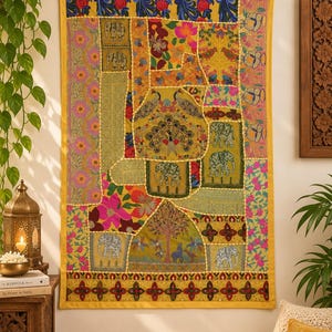 Peut inclure: Une tenture murale rectangulaire composée d'un assemblage de panneaux de tissu aux couleurs vives. Le textile présente des motifs brodés incluant des éléphants, des paons, des oiseaux et des fleurs, le tout encadré par une bordure jaune unie.