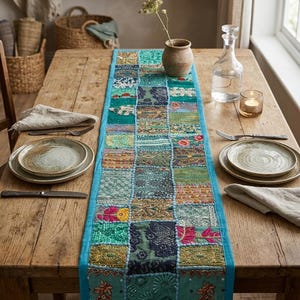 Pode incluir: Um caminho de mesa retangular com um design de patchwork de v&aacute;rios quadrados de tecido em tons de azul-turquesa, azul e dourado. Cada quadrado &eacute; decorado com bordados intrincados, lantejoulas e missangas. Possui uma borda lisa em turquesa.