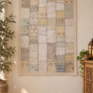 May include: A rectangular wall hanging featuring a patchwork design composed of various fabric squares in neutral tones including cream, beige, pale yellow, and soft grey. The textile displays intricate embroidery, lace, and floral patterns.