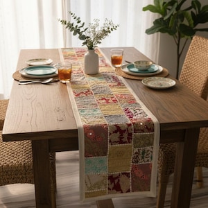Op de afbeelding: Een houten eettafel met een patchwork tafelloper in tinten rood, groen en goud. De tafel is gedekt met borden, glazen en een vaas met bloemen. De tafelloper bestaat uit een verscheidenheid aan patronen.
