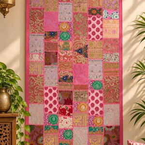 May include: A rectangular wall hanging featuring a patchwork design of various fabric squares in shades of pink, gold, green, and orange. The textile displays intricate embroidery, metallic thread accents, sequins, and floral patterns, all bordered by a solid pink fabric frame.