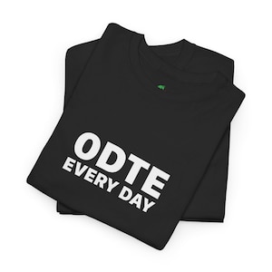 Puede incluir: Dos camisetas negras dobladas y apiladas. La camiseta superior muestra el texto blanco "ODTE EVERY DAY" en una fuente en negrita sin serifa. Las camisetas están hechas de un material suave, probablemente algodón o una mezcla de algodón.