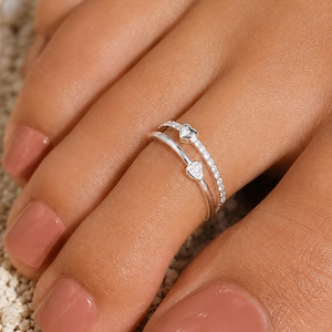 Peut inclure: Une bague d'orteil double en métal argenté ornée de deux petits motifs en forme de cœur. Un anneau est serti d'une rangée de minuscules pierres claires, tandis que l'autre présente un cœur lisse et un cœur incrusté de trois petites pierres.