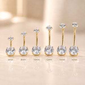 May include: Six gold-tone curved barbell navel rings with clear round-cut gemstones at each end. The bars are labelled with the word TITANIUM and lengths of 6mm, 8mm, 10mm, 12mm, 14mm, and 16mm are printed below each corresponding piece of jewellery.