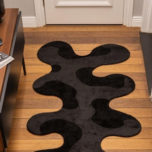 Irregular Black Hand-Tufted Wool Runner Rug with Abstract Wavy Shape, placed on a wooden floor in a modern entryway with stairs.