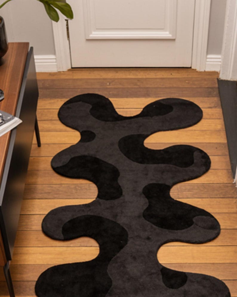 Irregular Black Hand-Tufted Wool Runner Rug with Abstract Wavy Shape, placed on a wooden floor in a modern entryway with stairs.