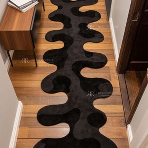 Irregular Black Hand-Tufted Wool Runner Rug with Abstract Wavy Shape, placed on a wooden floor in a modern entryway with stairs.