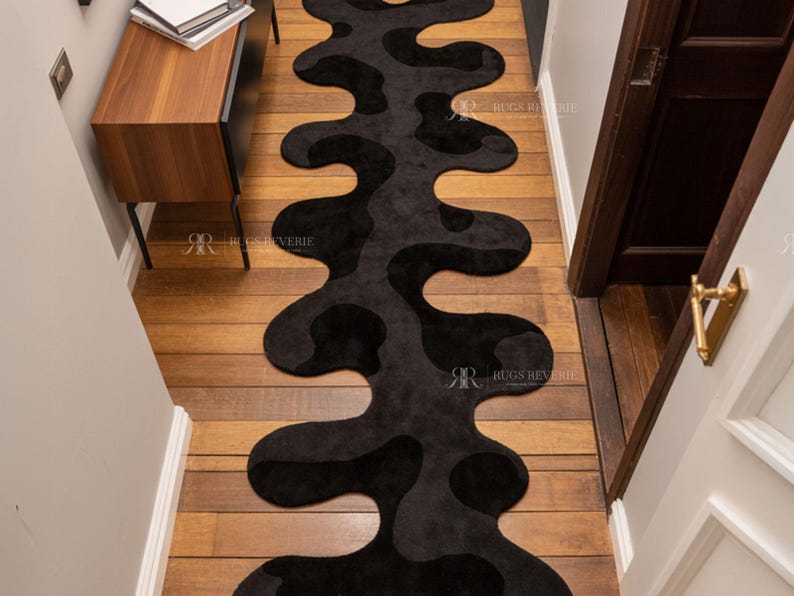 Irregular Black Hand-Tufted Wool Runner Rug with Abstract Wavy Shape, placed on a wooden floor in a modern entryway with stairs.