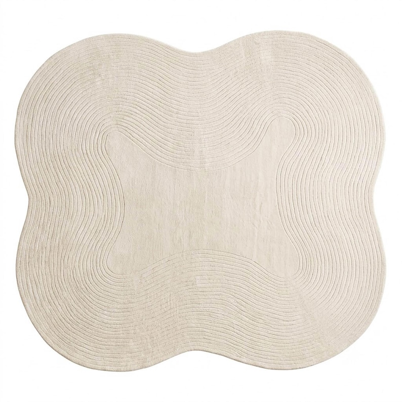May include: An off-white area rug with a distinct four-lobed, clover-like shape. The surface features a series of concentric, raised line patterns that follow the curved contours of the rug, creating a textured, ripple-like effect across the entire piece.